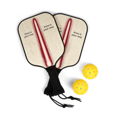 Two wooden pickleball paddles with black handles and a red and white striped design on the paddle faces, with text "Print it your way" on both sides of the stripe, next to two yellow pickleballs.