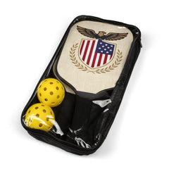 A black zippered travel case containing one wooden pickleball paddle and two yellow balls visible through the clear plastic front.